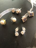 Three pairs of stud earrings and earring attachments on surface with a sheer white ribbon.