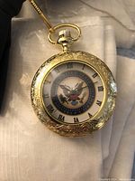 Gold-tone pocket watch with embossed design and Eagle emblem on dial