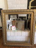 Overall photo showing large carved wooden frame and assortment of smaller frames on white brick hearth