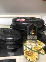 Photo showing two black granite ware pots with lids, two sunflower-patterned pot holders, and vintage wall hanging