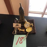 Photo showing all items arranged: Empire State Building statue, pocket watch, keychain, Spirit of '76 lapel pin, and tie pin.