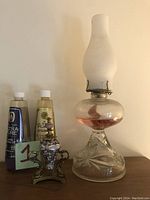 Full view of vintage glass oil lamp with frosted chimney, decorative dragonfly lamp, and two bottles of oil