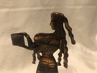 Side view of brass figure showing the woman holding an open box with detailed hair and garment texture, set against a plain light background.