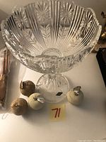 Full view of the clear cut crystal pedestal bowl with floral and geometric patterns, placed on a table and shown with decorative items nearby