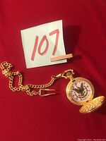 Full view of gold-tone pocket watch with chain and tie clip on red fabric background