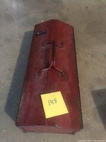Closed red metal tool box with two handles and a latch on top, showing some wear and surface rust.