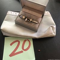Four rings in open jewelry box on white bag with green number 20 tag
