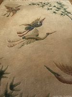 Close-up photo of the beige rug with embroidered or woven flying heron birds and green foliage pattern.