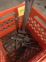 Photo of metal tools in a plastic crate showing a large sledgehammer with a wooden handle, multiple metal wedges, and several metal punches or chisels with wooden handles.
