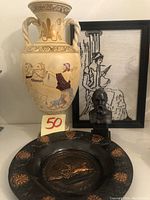 Photo showing tall hand painted Greek jar, small Socrates bust statue, framed embroidered Greek women art, and round black decorative plate with embossed golden designs.