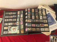 Partial open black collection book showing stamps of historical figures, birds, ships, and other themes.