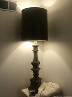 Full view of the large vintage lamp with black shade turned on, showing overall height and style.