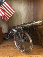 Close-up of decorative metal cannon on wood shelf, next to miniature American flags.