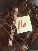 Wristwatch placed on top of the brown alligator skin clutch showing black face with diamond marker