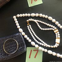 Two vintage white costume necklaces, one bracelet, and a small black change purse on a black background.