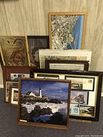 Multiple framed pictures arranged on floor against wall, including lighthouse photo, map or aerial photo, and historical railroad memorabilia.
