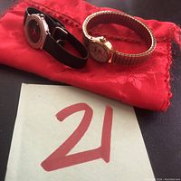 Two watches and red fabric pouch displayed on a flat surface