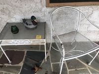 Front view of white wrought iron mesh chair and glass-topped wrought iron table with two duck figurines on table, showing condition and wear.