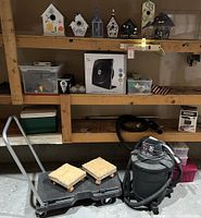 Display of Craftsman wet/dry shop vacuum, floor cart with padded supports, and boxed white box fan on garage shelving.