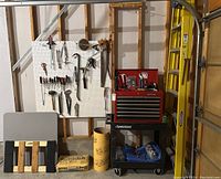 Wide view showing pegboard with hand tools, folding card table, bag of Quikrete concrete mix, cardboard tube and Husky tool cart with Craftsman toolbox