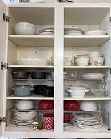 Cabinet shelves filled with various dinnerware items including bowls, plates, and glassware stacked and organized on wire racks.
