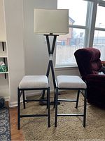 Front view of tall floor lamp and two metal frame fabric stools by window and chair