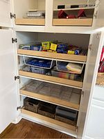 Kitchen cabinet shelves filled with plastic storage bins, baskets, kitchen supplies.
