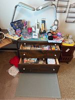 Large assortment of sewing and jewelry making supplies spread across a glass-topped wooden dresser, with drawers open showing more supplies. Includes threads, ribbons, small packages, and decorative doll.
