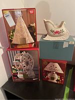 Four Lenox Christmas decor pieces shown outside and inside original boxes including a lighted Christmas tree, ceramic sleigh, lamp figurine, and Ferris wheel figurine.
