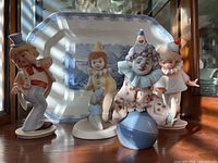 Four clown figurines displayed on a wooden surface with a blue and white plate backdrop under natural light