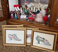 Miniature shoes displayed on a mirrored cabinet surface, with three framed shoe prints in front.