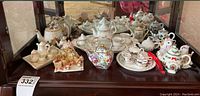 Full view of five porcelain miniature tea sets and various decorative teapots on bottom shelf of cabinet