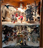 Two shelves in a wooden cabinet holding multiple Kachina dolls with fur, feathers, and painted details along with pottery pieces and a storyteller pottery vessel