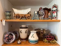 Two wooden shelves with an assortment of Native American pottery, figurines, miniature covered wagon, and red stagecoach models.