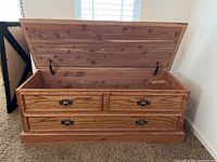 Front view of oak blanket chest with hinged lid open, showing interior cedar lining and two drawers with metal handles below.