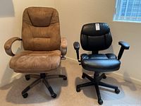 Two office chairs positioned side by side; left brown suede with padded armrests, right black leather with adjustable armrests and wheeled bases.