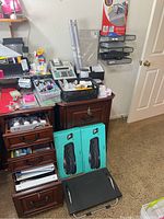 Photo showing two boxed Logitech MK550 wireless keyboard and mouse sets resting against a wooden desk, with drawers opened showing office supplies inside and additional office organizing trays and a filing rack on the wall.