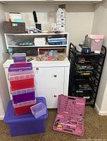Full view of storage bins in purple and red stacked, black drawer unit, white file cabinet with office supplies, and pink tool kit on the floor