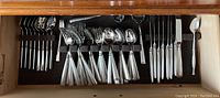 Full view of Oneida flatware set arranged in a wooden drawer organizer, showing forks, spoons, and knives with matching handle pattern.