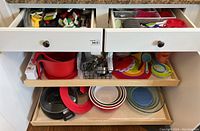 Photo showing drawers and lower cabinet with bowls and cups including red Pyrex bowl and colored rim glass bowls