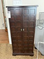 Front view of a tall, dark wood jewelry chest cabinet with paneled double doors and metal handles with sale tag visible.