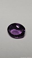 Close-up photo of deep purple oval amethyst gemstone, clear facets visible