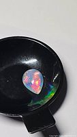 Pear-shaped cabochon fire opal placed on a black tray showing intense color play of orange, red, and yellow.