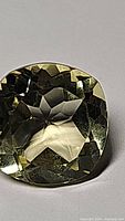 Close-up photo of natural cushion cut lemon citrine gemstone with yellow hue and clear facets.