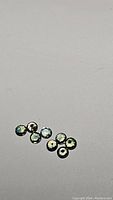 Eight small round faceted multicolored sapphires scattered on a flat light surface.