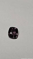 Close-up image of the 1.42ct cushion cut purple spinel gemstone on a grey white background, showing clarity and facet details.