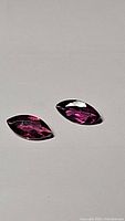 Pair of marquis cut pink-purple rhodolite garnet gemstones displayed on a plain light surface.