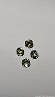 Four round cut bright green sapphires placed on a white background, showing size, shape, and color.