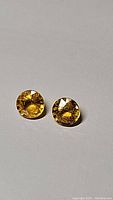 Close-up photo of two round deep canary yellow sapphires placed on a white/grey background, highlighting their rich yellow color and facets.