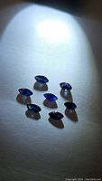 Seven marquis cut natural blue sapphires arranged on a white surface with spotlight illumination to show color and clarity.
